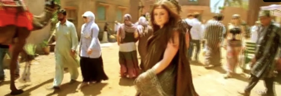 A woman walks through a sunlit market street with a camel at the left