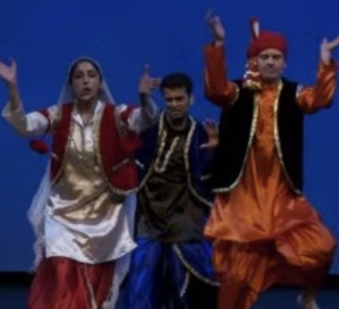 Three dancers performing in traditional costume against a blue stage backdrop